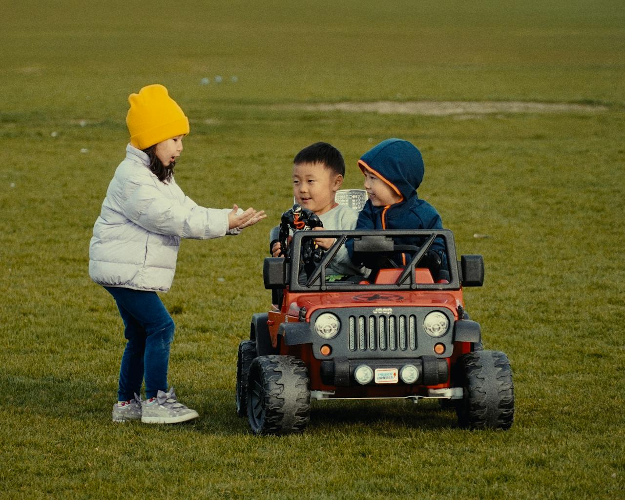 Three children enjoy a sunny day with a toy jeep in an Oakville, Ontario park.