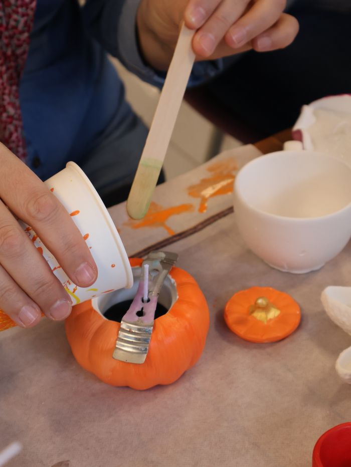services-04 A person crafting a pumpkin candle with melted wax during a Halloween themed activity.