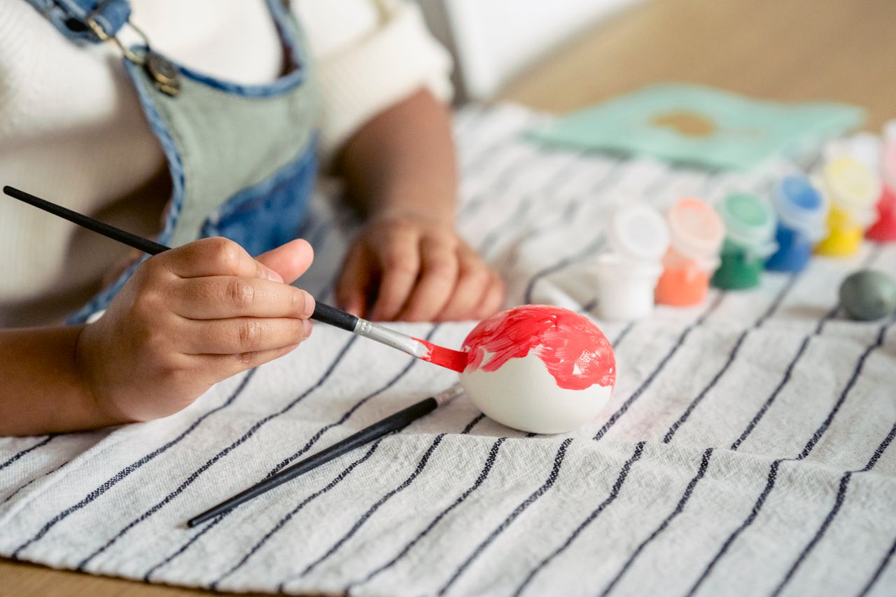 Child painting an Easter egg on a table, engaging in a creative art and craft activity.