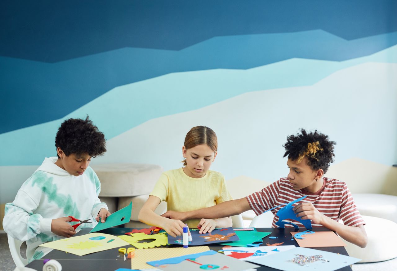 services-01 Children engaged in a craft activity with paper and scissors indoors, showcasing creativity and teamwork.